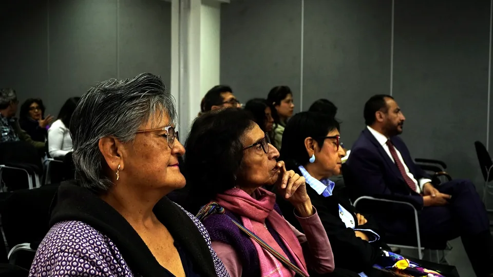 Público asistente al congreso observa la exposición desde sus asientos en una sala cerrada.