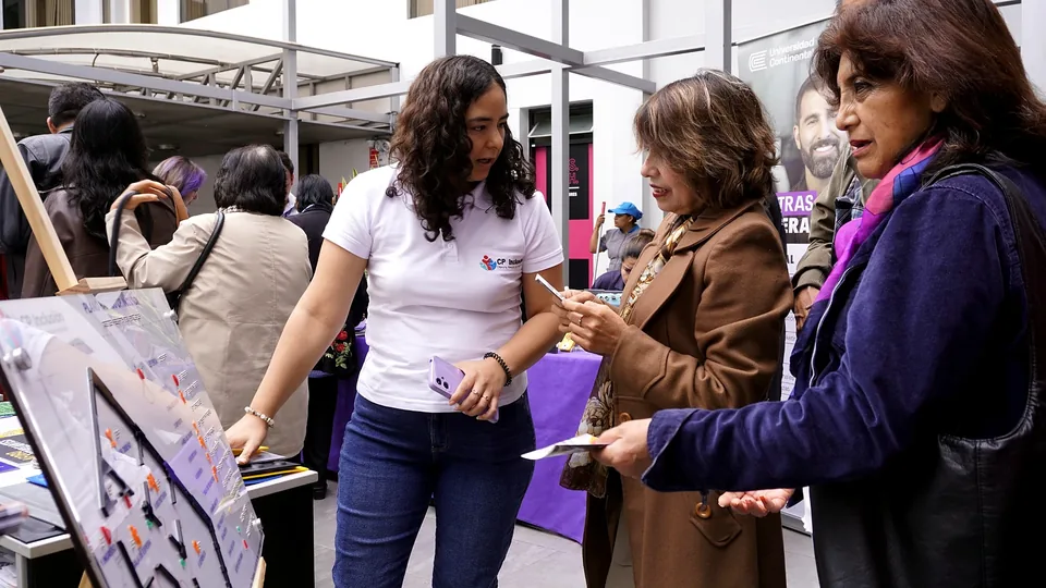 En un patio interior, una expositora muestra un plano háptico a dos asistentes durante una actividad del evento.