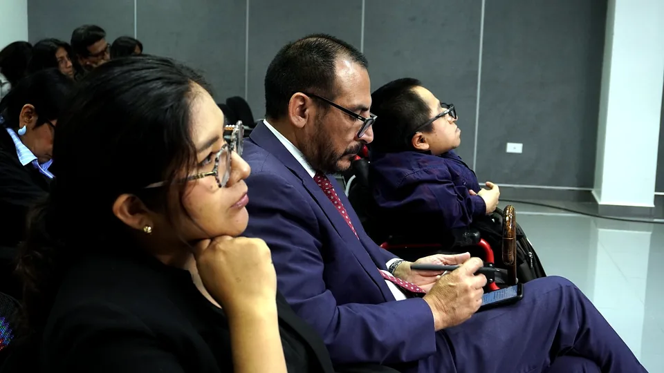 Asistentes, incluida una persona usuaria de silla de ruedas, siguen la ponencia desde la primera fila.