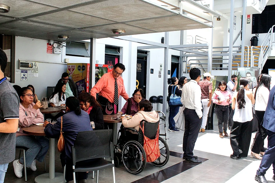 Asistentes del congreso conversan y comparten un refrigerio en el patio interior del recinto; en primer plano se observa una participante usuaria de silla de ruedas.