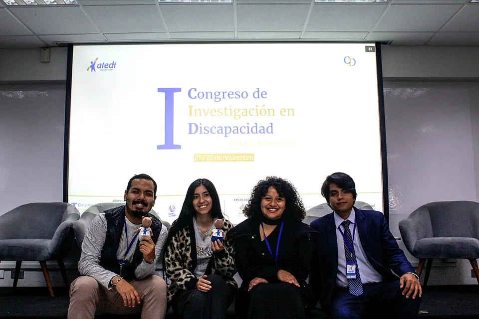 Cuatro participantes posan sonrientes en el escenario del congreso frente a la pantalla principal.