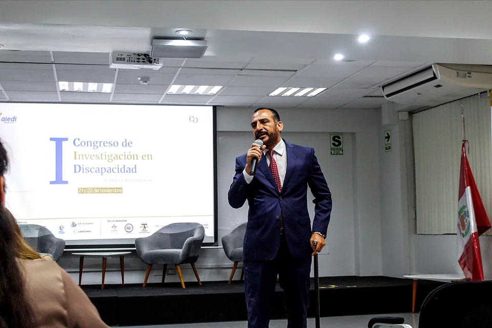 Un expositor con traje oscuro ofrece una intervención desde el auditorio con el escenario del congreso al fondo.