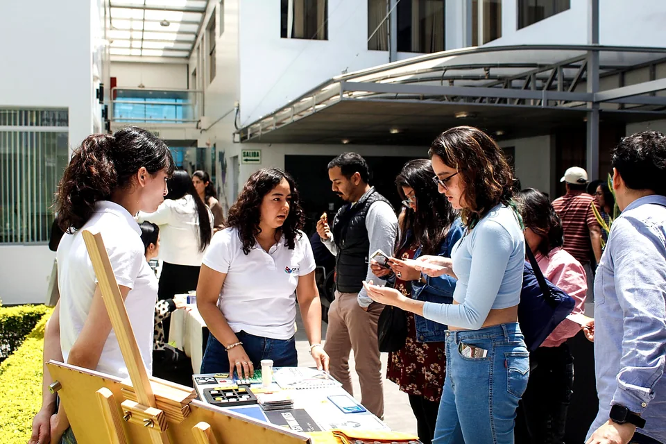 Varias asistentes visitan una mesa informativa instalada en el patio del evento y revisan materiales de difusión.