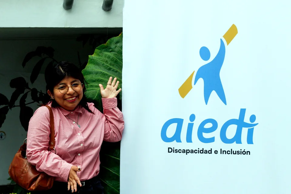 Participante sonriendo junto a un panel con el logo institucional de AIEDI – Discapacidad e Inclusión.