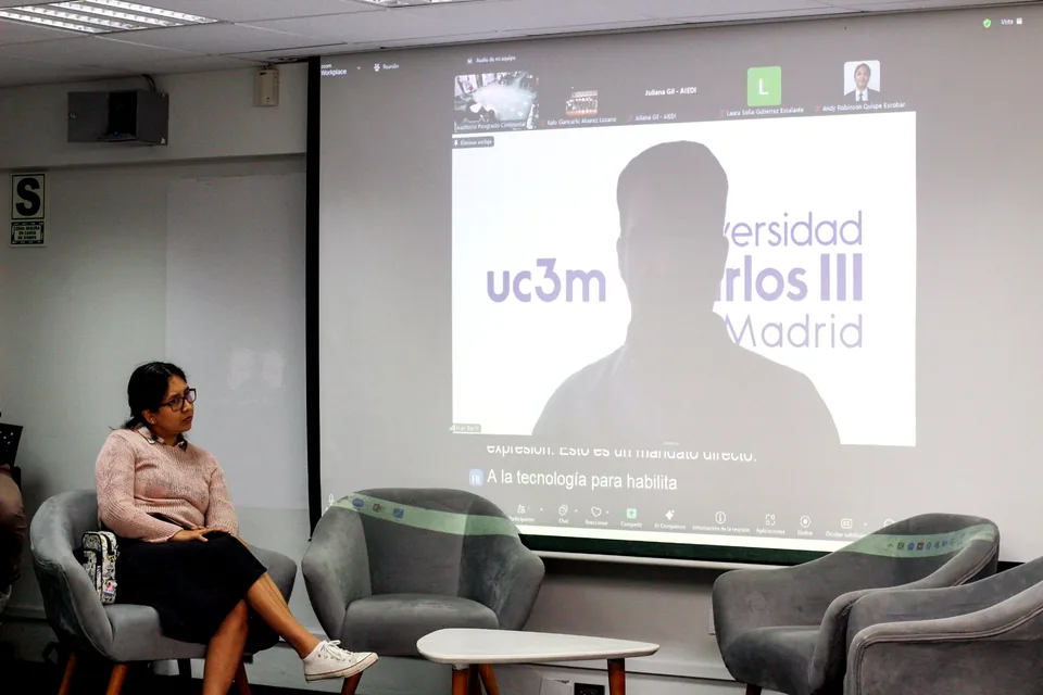 Participante sentada en un panel académico mientras se proyecta en pantalla una intervención virtual de la Universidad Carlos III de Madrid.