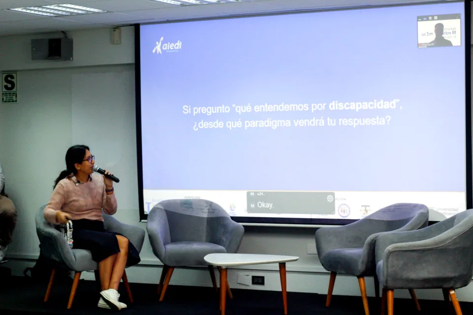 Participante exponiendo con micrófono frente a una diapositiva de AIEDI durante un panel sobre discapacidad.